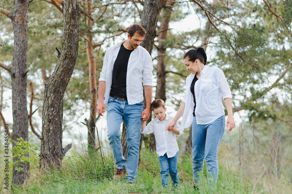 Mom, dad and son walk in the green grass. Happy young family spending time together, running outside, go in nature, on vacation, outdoors. The concept of family holiday.
