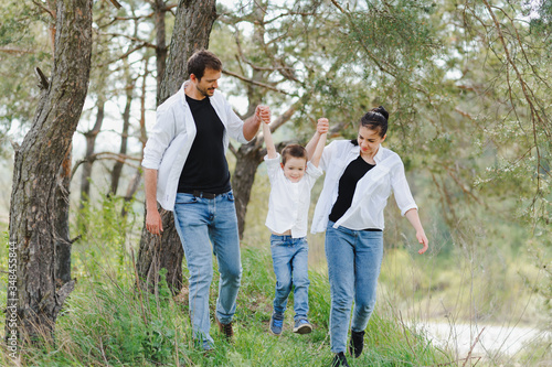 Mom, dad and son walk in the green grass. Happy young family spending time together, running outside, go in nature, on vacation, outdoors. The concept of family holiday. © Serhii