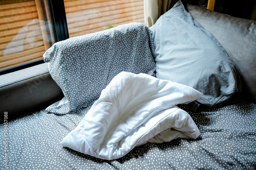 Grey pokadot pillow and grey set with fold white blanket was used left on Messy sofa next to window with sunshine,cover sheet on sofa be crumpled,Disorder and mess at home.