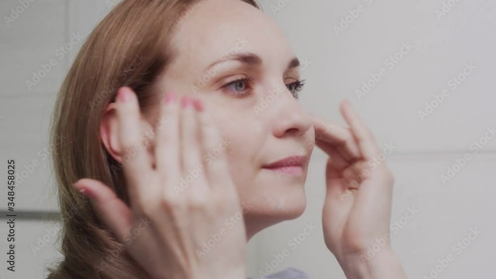 Adult woman applying cream and looking in mirror Adult woman applying cream and looking in mirror