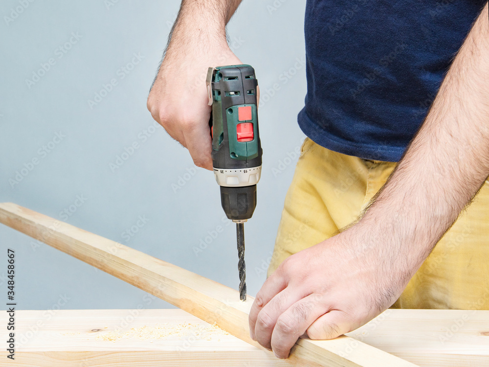 A handyman drills a wooden rail. Men's hands at work.
