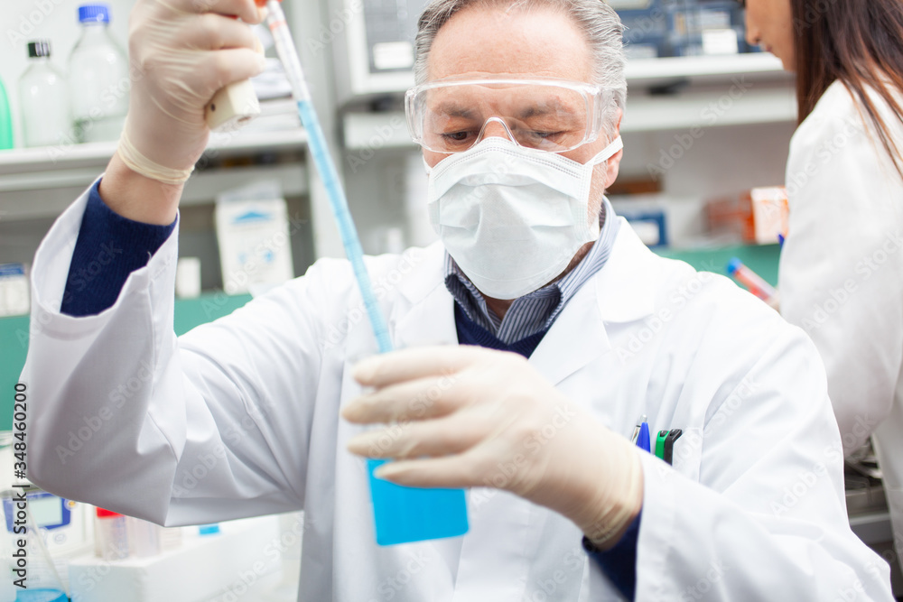 Researcher holding flask with blue liquid in the lab, coronavirus research concept Researcher holding flask with blue liquid in the lab, coronavirus research concept