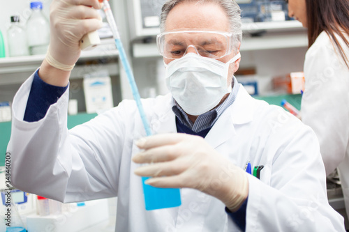 Researcher holding flask with blue liquid in the lab, coronavirus research concept