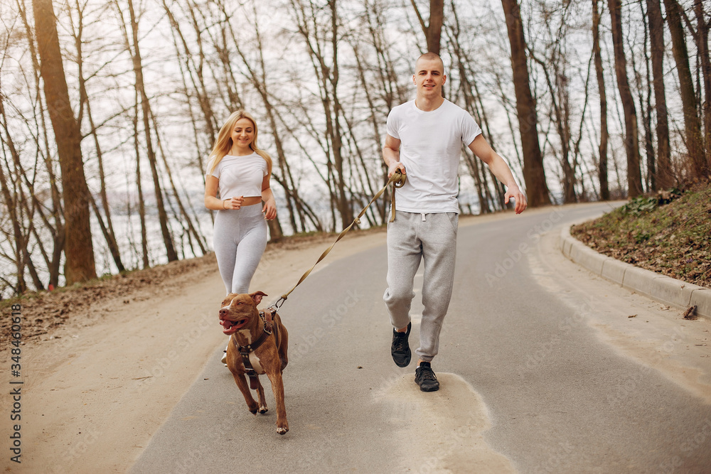 Obraz premium Beautiful couple in a park. Sportsman in a sportswear. Couple with a dog
