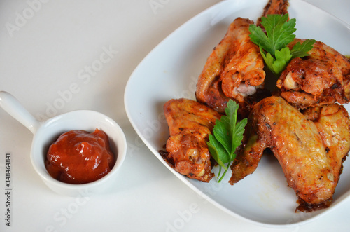 plate of chicken wings on white table red sauce in a gravy boat