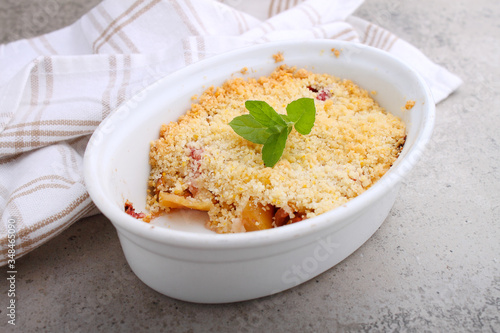 Crumble with strawberries and apples on a white plate and concrete background.