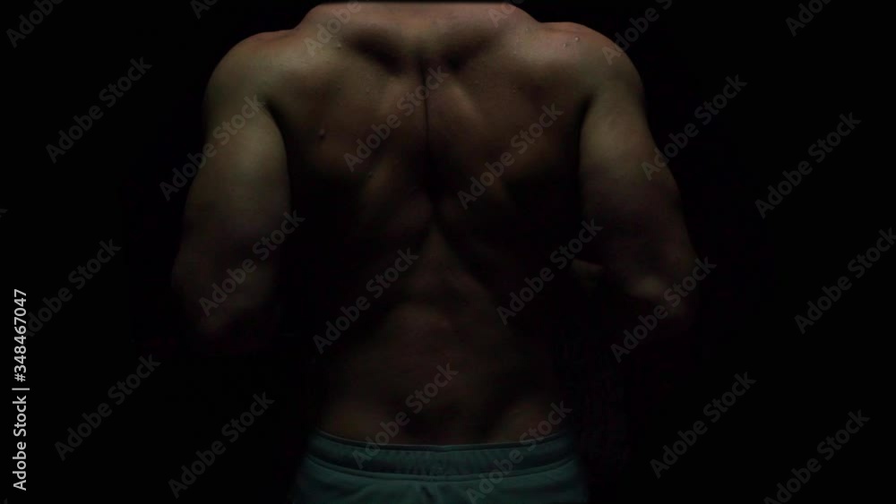 a pumped-up man shows the muscles of his back on a black background without a T-shirt a pumped-up man shows the muscles of his back on a black background without a T-shirt