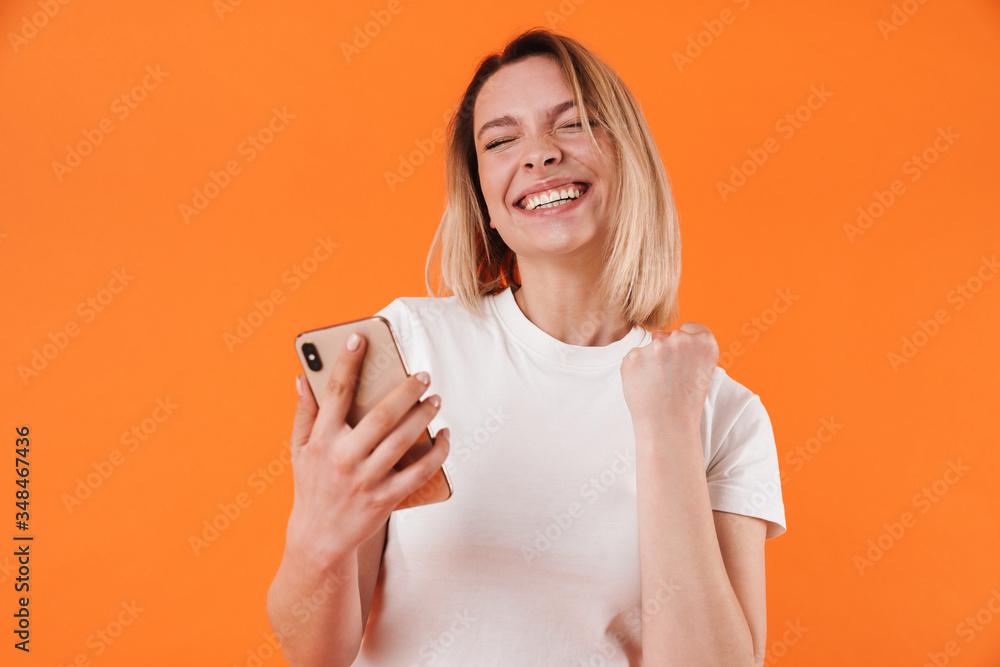Image of delighted woman making winner gesture while using mobile phone Image of delighted woman making winner gesture while using mobile phone