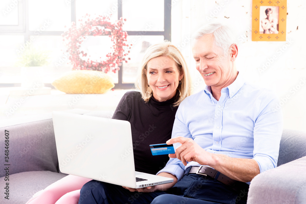 Senior couple using bank card and laptop while shopping online from home