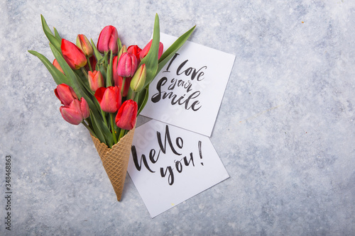 red  beautiful tulips in an ice cream waffle cone with card Hello you on a concrete background. Conceptual idea of a flower gift. Spring mood