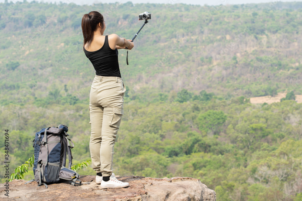 Fototapeta premium A woman taking a selfie on a cliff at the top of the hill