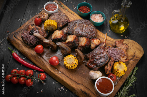 Assorted delicious grilled meat with vegetable and herbs on rustic table
