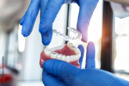 The doctor’s hands in blue gloves hold an artificial model of the jaw with invisible braces. The dentist shows an example of tooth alignment. photo