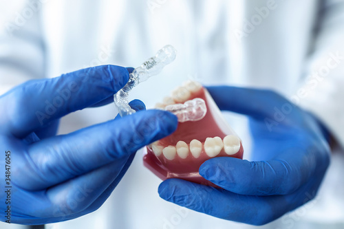 The doctor’s hands in blue gloves hold an artificial model of the jaw with invisible braces. The dentist shows an example of tooth alignment. photo