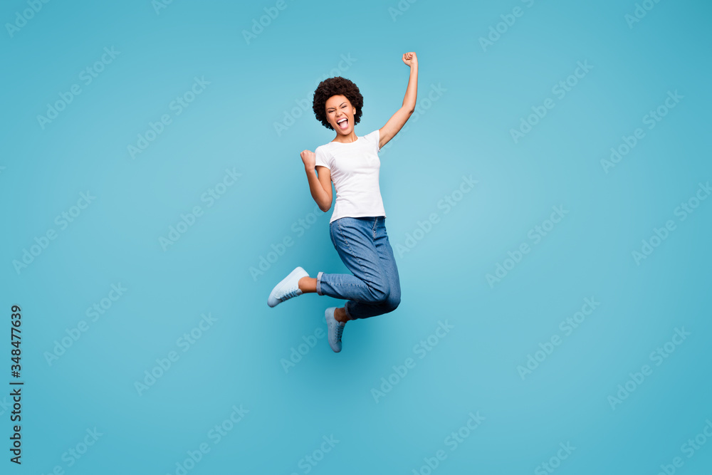 Full length photo of ecstatic dark skin wavy lady jumping high sporty competitive person celebrating goal match fan wear casual white t-shirt jeans isolated blue color background - obrazy, fototapety, plakaty 