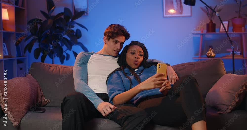 Cheerful mixed race couple making selfies while sitting on couch. Young woman with dreadlocks and her cute boyfriend posing while making photos and spending time at home Cheerful mixed race couple making selfies while sitting on couch. Young woman with dreadlocks and her cute boyfriend posing while making photos and spending time at home