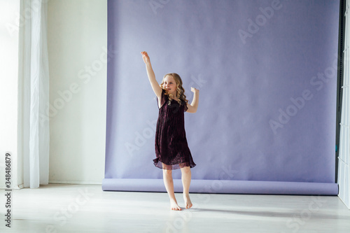 Fototapeta Naklejka Na Ścianę i Meble -  Beautiful little girl in dress dances alone at home