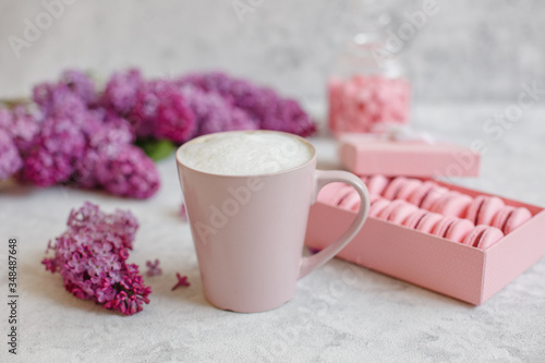 coffee mug, macaroons in a box blooming branch of lilac lie on a gray background
