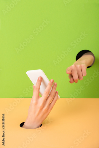 cropped view of woman pointing with finger and holding smartphone on green and orange