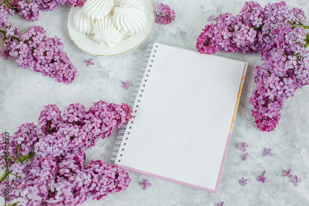a clean Notepad, meringue blooming branch of lilac lie on a gray background a clean Notepad, meringue blooming branch of lilac lie on a gray background