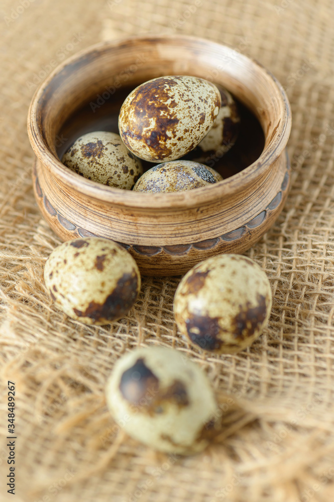 Quail eggs and a clay bowl on a cloth made of sacking. Rustic still life with quail eggs. Small colorful quail eggs close-up. Quail eggs and a clay bowl on a cloth made of sacking. Rustic still life with quail eggs. Small colorful quail eggs close-up.