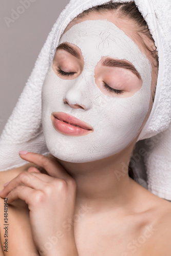 Beauty portrait of woman in towel on head with white nourishing mask or creme on face, white background isolated. Skincare cleansing eco organic cosmetic spa relax concept