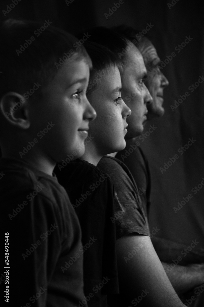 Two sons, father and grandfather in profile against a dark background. Two children and two adults of European race in profile on black and white photograph. Three male generations. Two sons, father and grandfather in profile against a dark background. Two children and two adults of European race in profile on black and white photograph. Three male generations.