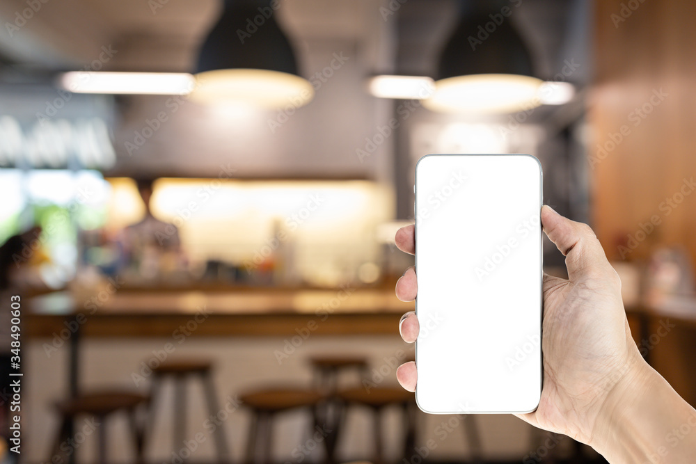Mockup image of hand holding white mobile phone with blank white screen, blurred cafe background. Mockup image of hand holding white mobile phone with blank white screen, blurred cafe background.
