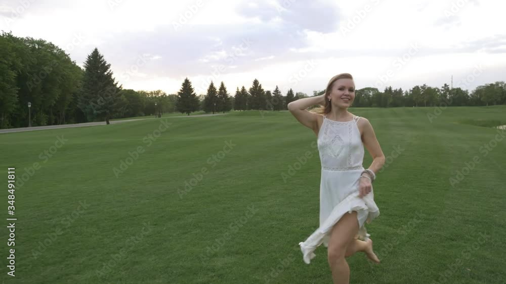 Beautiful blonde girl in a white dress runs and dances barefoot on the green grass in summer day Beautiful blonde girl in a white dress runs and dances barefoot on the green grass in summer day