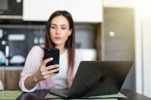 Young Woman reading on her mobile phone and smiling while use laptop at home.