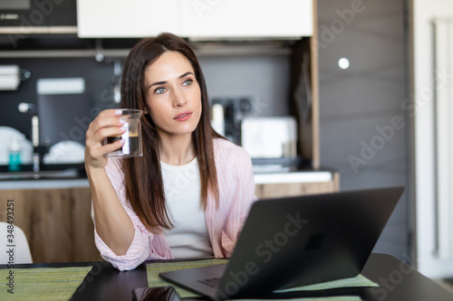 Young woman with coffee cup and laptop in the kitchen at home