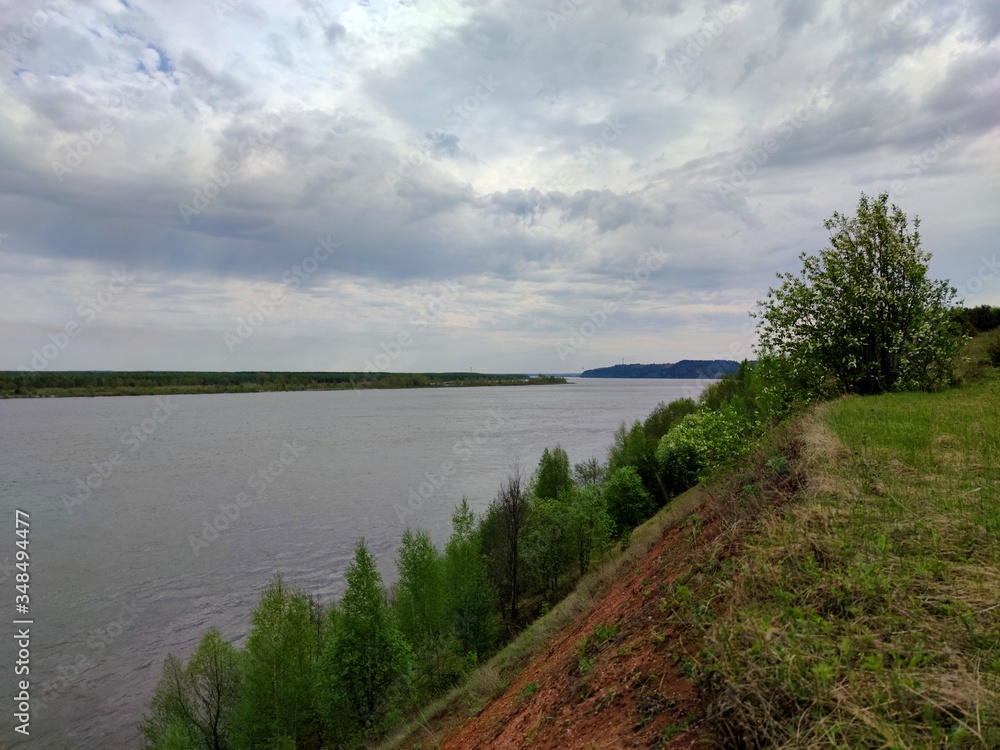 trees on a slope near the river against a gloomy sky with clouds before the rain