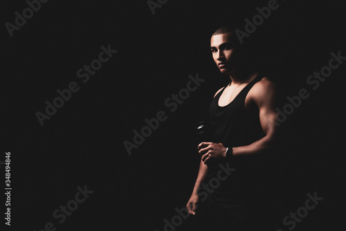 Muskulöser Mann mit Trinkflasche vor schwarzem Hintergrund 