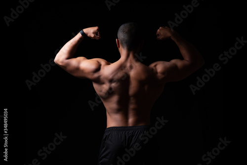 Ein Mann mit muskulösem Rücken vor schwarzem Hintergrund, angespannte Rückenmuskulatur 