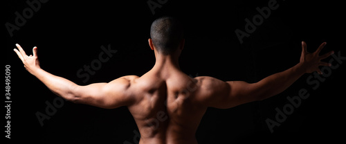 Ein Mann mit muskulösem Rücken vor schwarzem Hintergrund, angespannte Rückenmuskulatur 