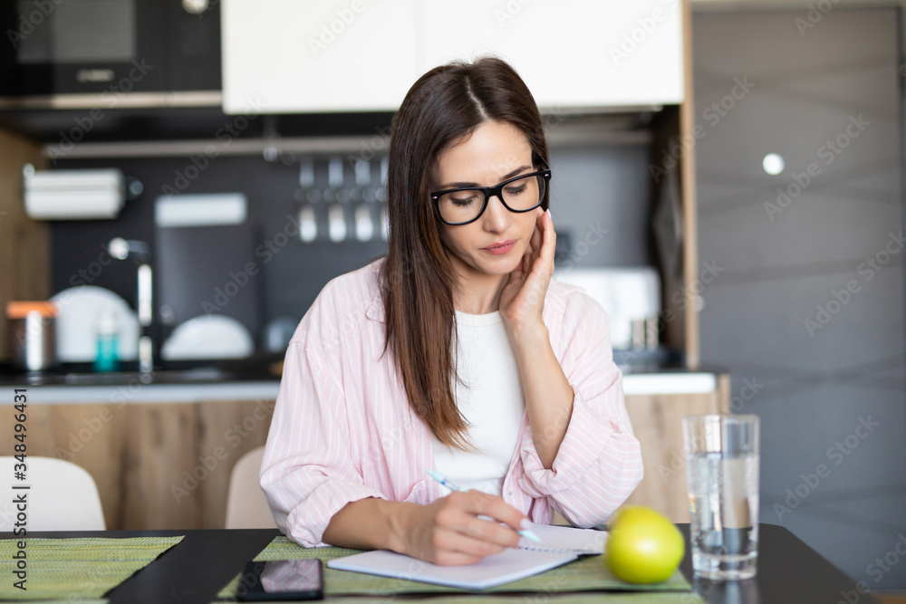 Smiling woman writing on note pad in the kitchen Smiling woman writing on note pad in the kitchen