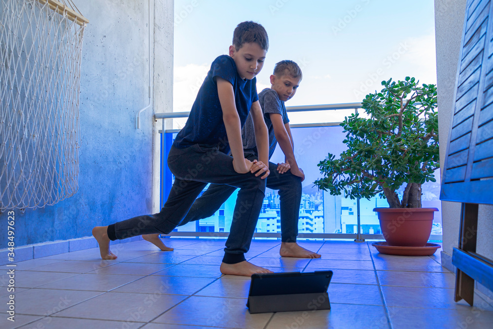 Fototapeta premium Chłopcy z komputera typu tablet robi ćwiczenia sportowe na balkonie. Sport, zdrowy tryb życia, aktywny wypoczynek w domu