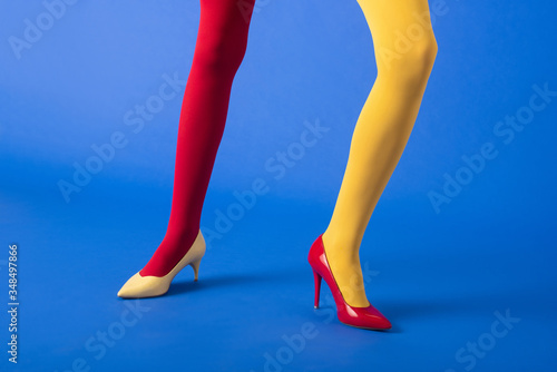 cropped view of woman in yellow and red tights and heels posing on blue