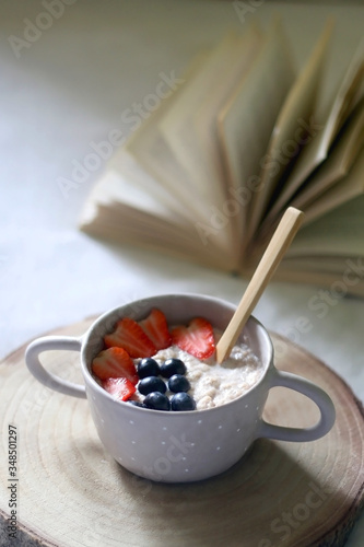 Bowl of porridge with fruit and open book on a bed. Selective focus.