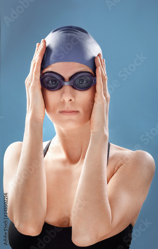 Portrait of female swimmer with cap and goggles on blue background