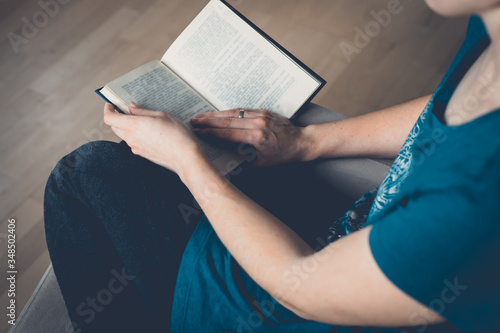 A young pretty woman sits on an armchair and reads a book.Close-up of female hands holding an open book. Cozy home