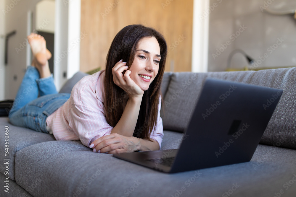 Beautiful woman with happy smile lying on the sofa with laptop Beautiful woman with happy smile lying on the sofa with laptop