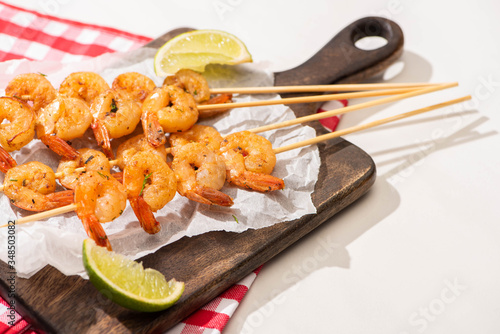 prawns on skewers with lime on parchment paper on wooden board and plaid napkin on white background