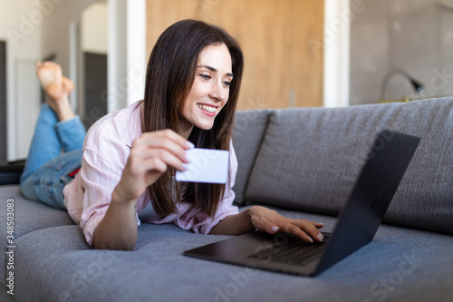 Young woman entering her credit card numbers on a website while lying on a sofa. Shopping online.