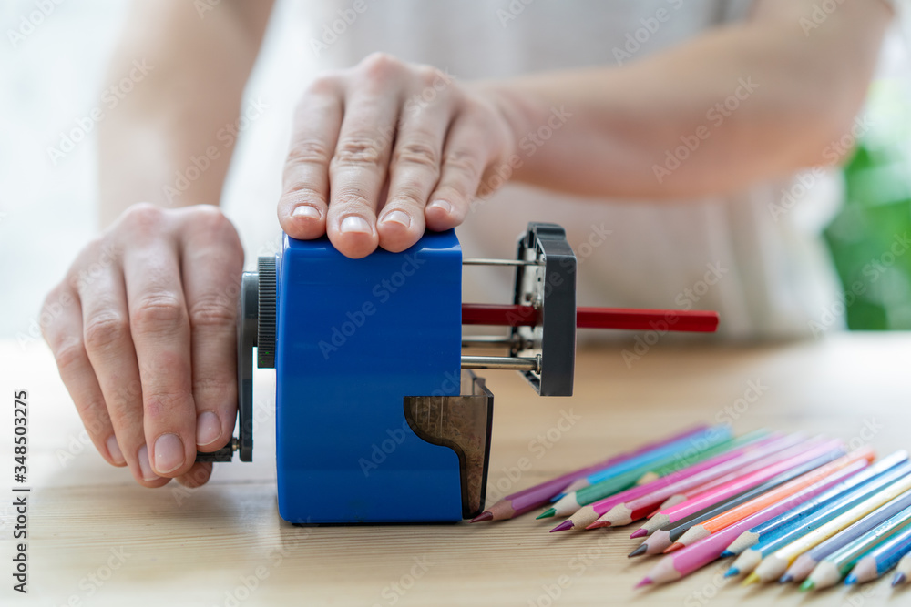 Obraz premium close-up of women's hands using a blue pencil sharpener at the table, school concept