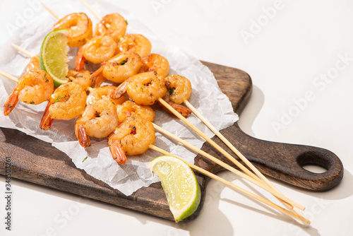 prawns on skewers with lime on parchment paper on wooden board on white background