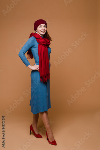 Beautiful caucasian female with medium dark hair in blue dress, red hat and red scarf