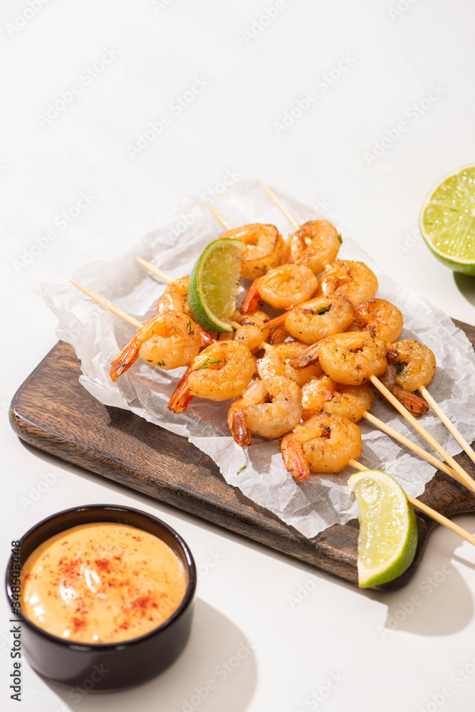 prawns on skewers with lime and sauce on parchment paper on wooden board on white background prawns on skewers with lime and sauce on parchment paper on wooden board on white background