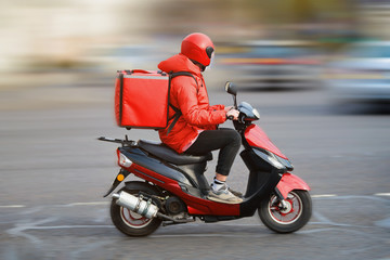 Food delivery moto scooter driver with red backpack behind back is on his way to deliver food. Courier on scooter delivering food. Quick shipping of goods to customers