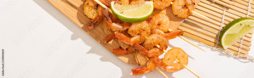 top view of prawns on skewers with lime on bamboo mat on white background, panoramic orientation top view of prawns on skewers with lime on bamboo mat on white background, panoramic orientation